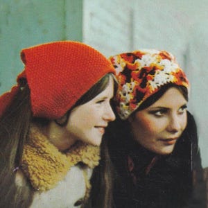 May include: Two women wearing knitted and crocheted hats. One hat is a solid orange color, and the other is a mix of white, orange, and brown. The women are smiling and looking to the side.