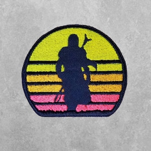 May include: Embroidered patch featuring a silhouette of a figure in a hooded cloak standing in front of a retro sunset with yellow, orange, and pink stripes.