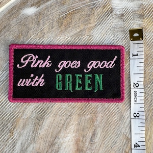 Op de afbeelding: Roze en groene geborduurde patch met de tekst "Pink goes good with GREEN".