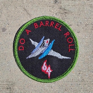 May include: Round black patch with green trim featuring a stylized spaceship and the text "DO A BARREL ROLL" in red. The number "64" is in red below the spaceship.