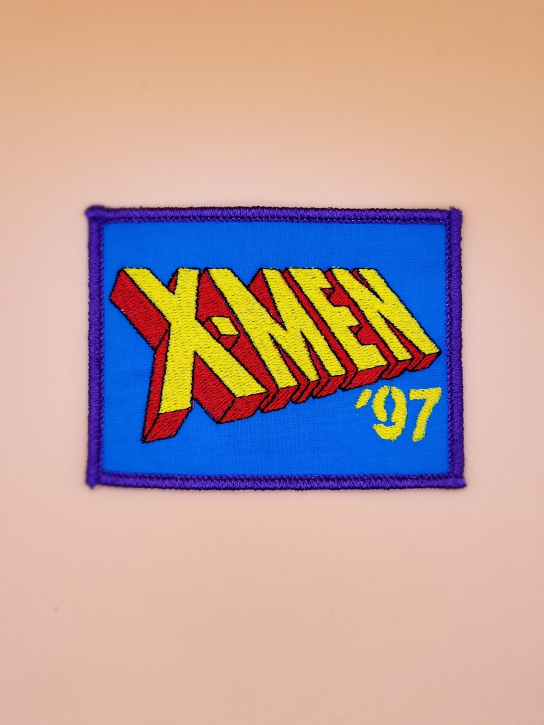Może przedstawiać: Naszywka haftowana w kolorze niebieskim i fioletowym z napisem "X-MEN '97" w ż&oacute;łtych i czerwonych literach.