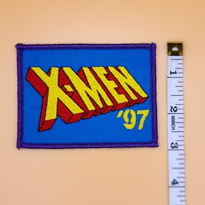 Może przedstawiać: Niebieska naszywka haftowana z napisem "X-Men '97" w ż&oacute;łtych i czerwonych literach.