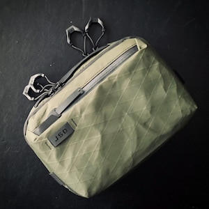 May include: A green quilted zippered pouch with a black JSD label. The pouch has a zippered pocket on the front and a silver zipper pull.