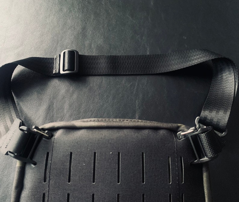 May include: A black crossbody bag with a black adjustable strap and silver buckles. The bag has a textured front panel with multiple rows of small holes.