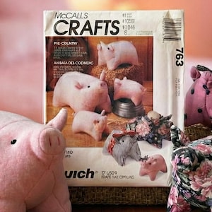 May include: A collection of handmade pig-shaped crafts, including pink felt pigs and patterned fabric pigs. A McCall's Crafts pattern is visible, suggesting a DIY sewing project. The scene is set on a wooden surface with a pink-themed background.