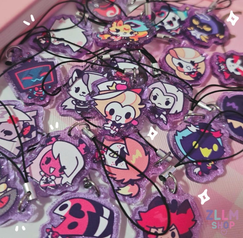 May include: A collection of purple glittery acrylic charms featuring various cartoon character designs. Each charm has a black lanyard attached. The charms are in various shapes and sizes, with a variety of colors and designs.