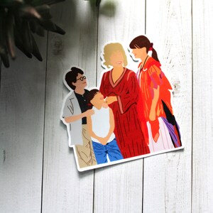 May include: A sticker featuring a group of four people, two women and two children. The women are wearing red and orange clothing, and the children are wearing blue and white clothing. The sticker is on a white wooden background.