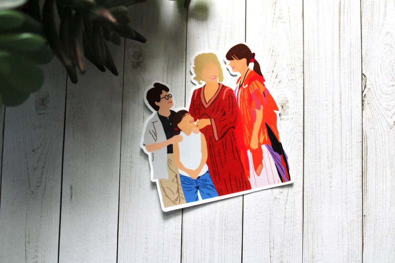 May include: A sticker featuring a group of four people, two women and two children. The women are wearing red and orange clothing, and the children are wearing blue and white clothing. The sticker is on a white wooden background.
