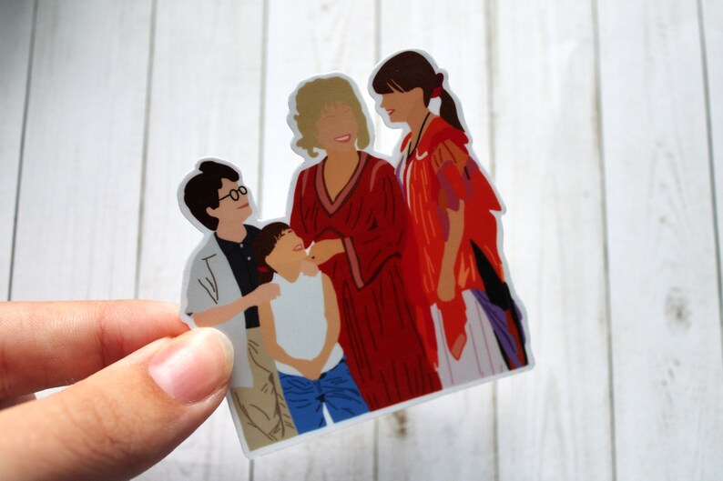 May include: A sticker featuring a group of four people, two adults and two children. The adults are wearing red and purple clothing, while the children are wearing white and blue clothing. The sticker is on a white wooden background.