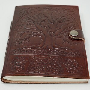 Puede incluir: Diario de cuero marr&oacute;n con un dise&ntilde;o de &aacute;rbol de la vida y un nudo celta. El diario tiene un cierre de correa con un bot&oacute;n de metal.
