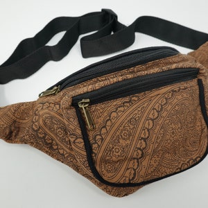 Op de afbeelding: Een bruine heuptas met een zwart paisley-patroon en een zwarte verstelbare riem. De tas heeft twee vakken met rits.