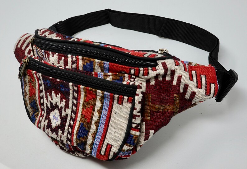 May include: A multi-coloured fanny pack with a black adjustable strap and two zippered compartments. The fabric features a geometric pattern in shades of red, blue, white, and brown.