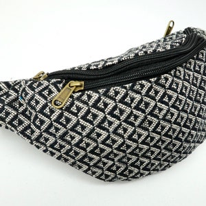 May include: Black and white patterned bum bag with a zipper closure. The bum bag is made of a woven fabric.