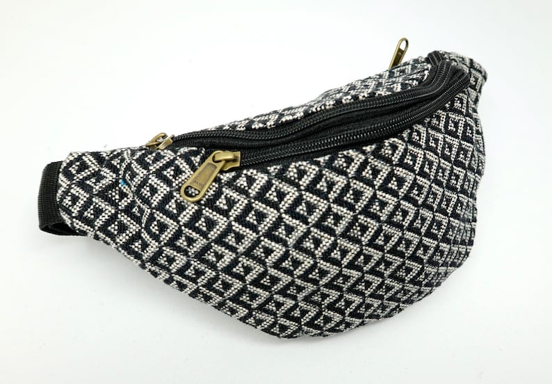May include: Black and white patterned bum bag with a zipper closure. The bum bag is made of a woven fabric.