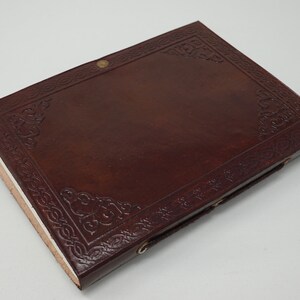 Puede incluir: Un diario de cuero marr&oacute;n con un dise&ntilde;o de nudo celta en relieve en la portada. El diario tiene un cierre sencillo con una correa de cuero y cierres met&aacute;licos.