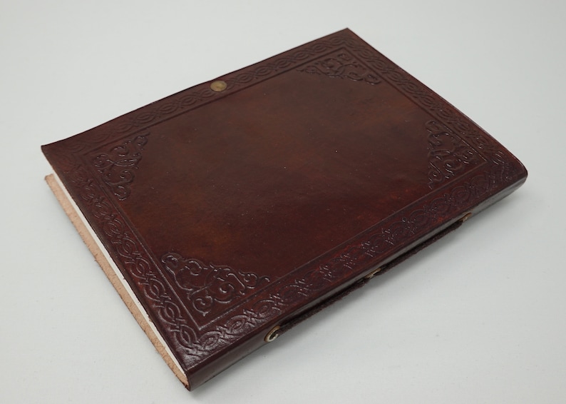 Puede incluir: Un diario de cuero marr&oacute;n con un dise&ntilde;o de nudo celta en relieve en la portada. El diario tiene un cierre sencillo con una correa de cuero y cierres met&aacute;licos.