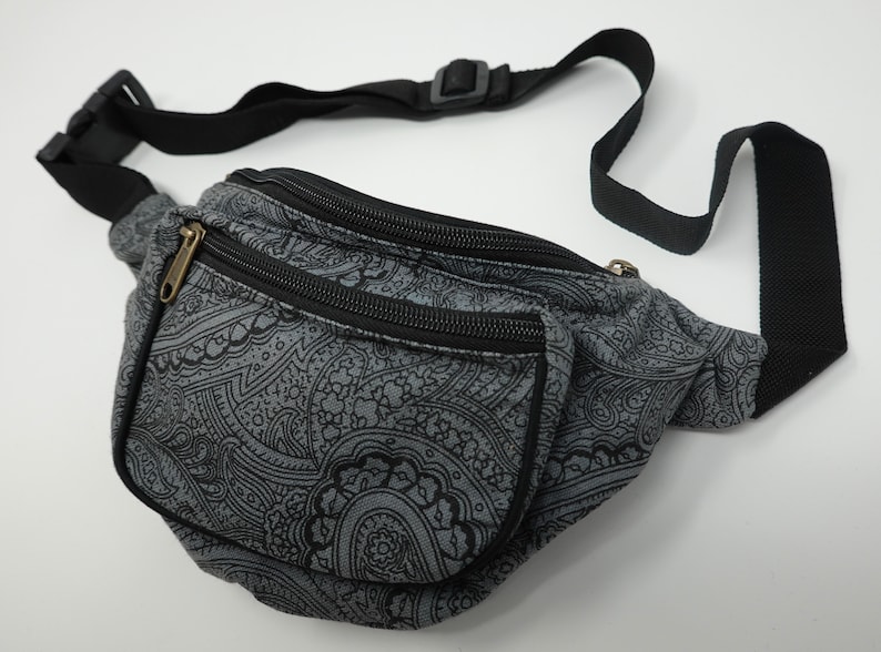 Op de afbeelding: Een grijze heuptas met een zwart paisley-patroon en twee ritsvakken. De heuptas heeft een zwarte verstelbare band.