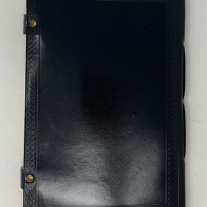 May include: Black leather journal with a Celtic knot border and brass accents. The journal has a flap closure with a brass button.