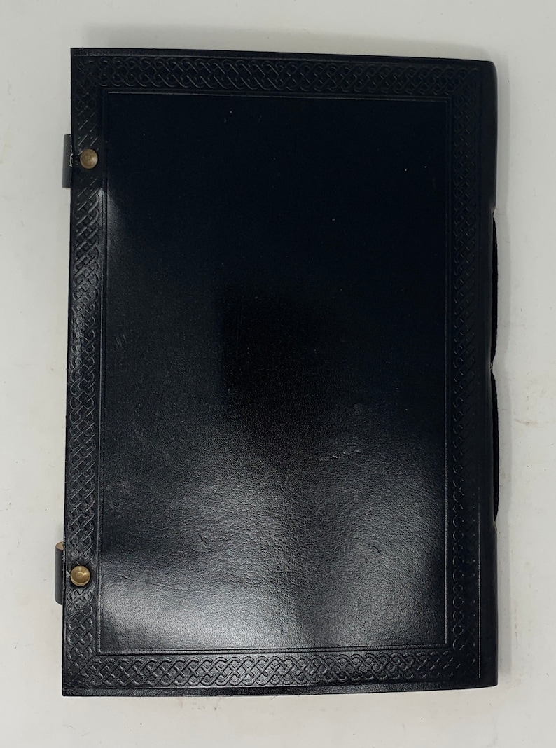 May include: Black leather journal with a Celtic knot border and brass accents. The journal has a flap closure with a brass button.