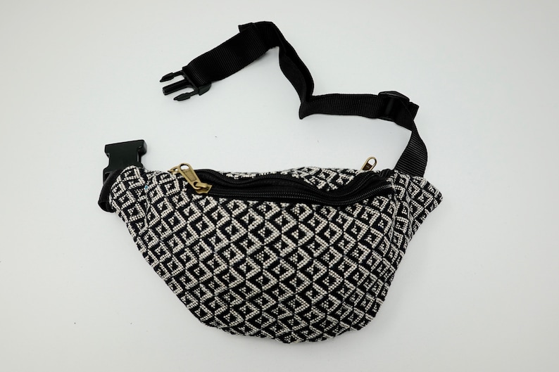 May include: Black and white geometric patterned fanny pack with a black adjustable strap and a gold zipper.