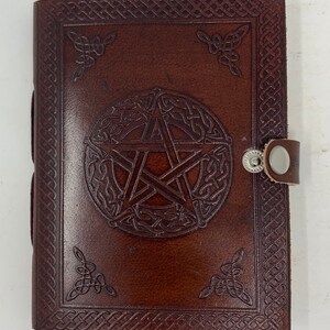 May include: Brown leather journal with a pentacle design embossed on the front cover. The journal has a Celtic knot border and a silver clasp.