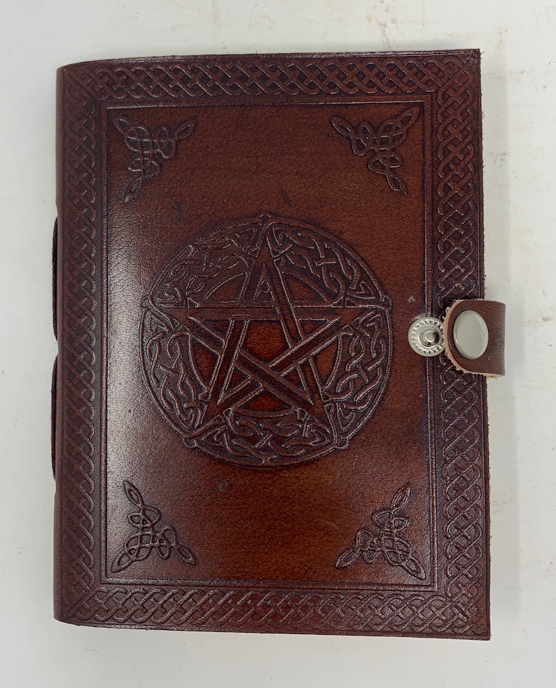 May include: Brown leather journal with a pentacle design embossed on the front cover. The journal has a Celtic knot border and a silver clasp.