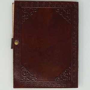 Puede incluir: Un diario de cuero marr&oacute;n con un borde decorativo en relieve y un cierre de lat&oacute;n. El diario tiene una portada en blanco.
