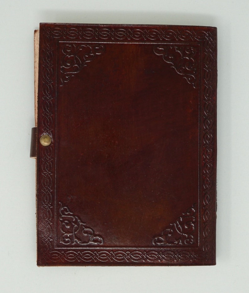 Puede incluir: Un diario de cuero marr&oacute;n con un borde decorativo en relieve y un cierre de lat&oacute;n. El diario tiene una portada en blanco.