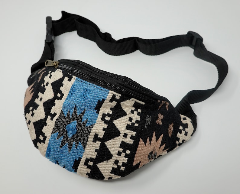 Pu&ograve; includere: Una marsupio nera con una tracolla regolabile. La marsupio ha una chiusura a zip ed &egrave; realizzata in tessuto intrecciato con un motivo geometrico in tonalit&agrave; di blu, nero, bianco e marrone.