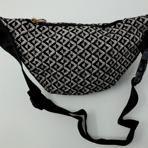 May include: Black and white patterned bum bag with a black adjustable strap. The bum bag has a zipper closure.