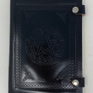 May include: Black leather journal with a pentagram design embossed on the front cover. The journal has a Celtic knot border and two metal clasps.