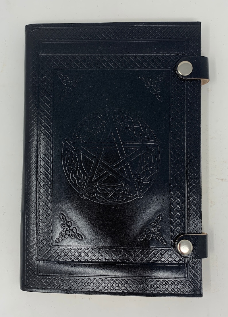 May include: Black leather journal with a pentagram design embossed on the front cover. The journal has a Celtic knot border and two metal clasps.
