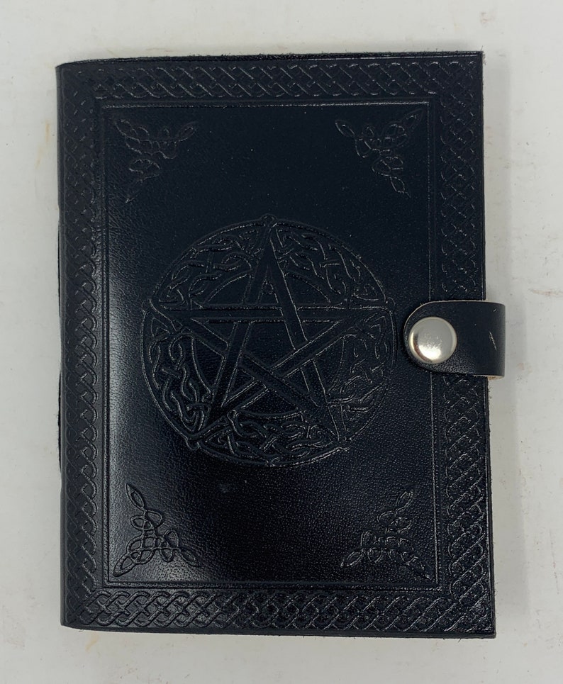 May include: Black leather journal with a pentagonal star design embossed on the front cover. The journal has a decorative border and a silver clasp.