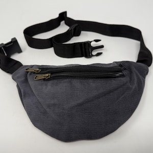 May include: A gray corduroy fanny pack with a black adjustable strap and two zippered compartments.