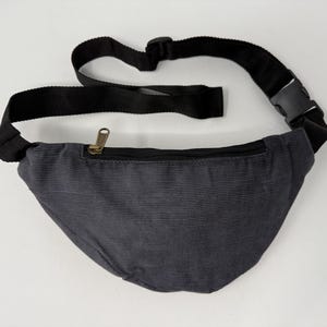 May include: A dark gray corduroy fanny pack with a black adjustable strap and a gold zipper.