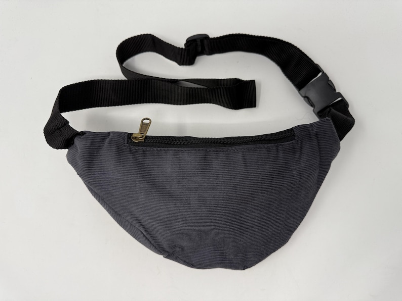 May include: A dark gray corduroy fanny pack with a black adjustable strap and a gold zipper.