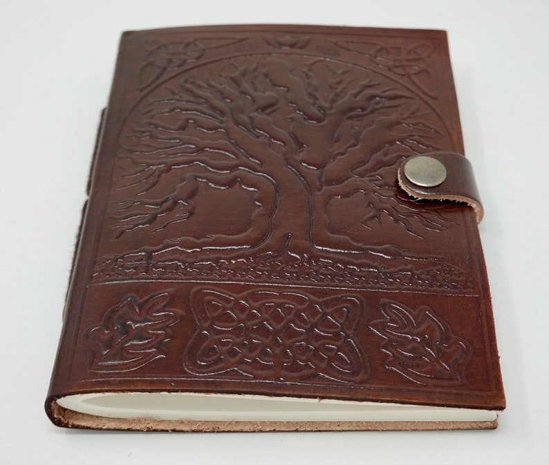 Puede incluir: Diario de cuero marr&oacute;n con un dise&ntilde;o de &aacute;rbol de la vida y un nudo celta. El diario tiene un cierre de correa con un bot&oacute;n de metal.
