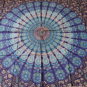 Puede incluir: Un tapiz con un gran diseño de mandala circular en tonos azules, verdes y marrones. El mandala está rodeado por un patrón floral más pequeño.