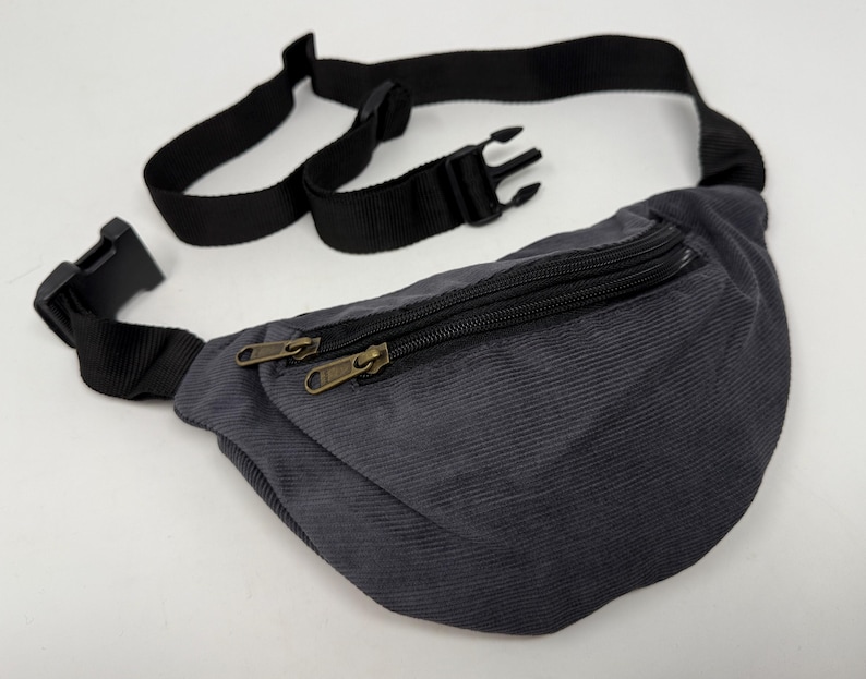 May include: A gray corduroy fanny pack with a black adjustable strap and two zipper closures.