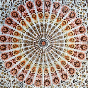 Pode incluir: Uma tapeçaria branca com um design de mandala marrom e laranja. A mandala tem um padrão circular com detalhes intrincados.
