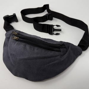 May include: A dark gray corduroy fanny pack with a black adjustable strap and two zippered compartments.
