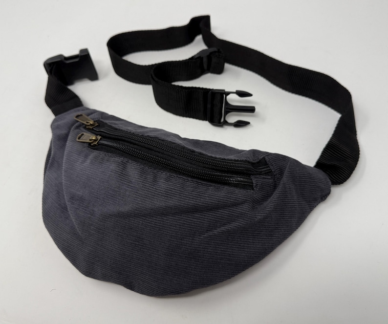 May include: A dark gray corduroy fanny pack with a black adjustable strap and two zippered compartments.