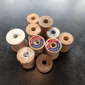 May include: A collection of eight wooden spools of thread, some with labels. The labels include the text "COATS & CLARKS", "MERCERIZED SEWING", "BUTTON BUTTONHOLE TWIST", "SHADE BLACK", "20c", "DRAGON", "THREE", "50", "THELDING", "125", "90", "POLY-BOND", "S & CLARKS", "COATS", "SEWING", "MERCERIZED", "4", "160", "INREE".