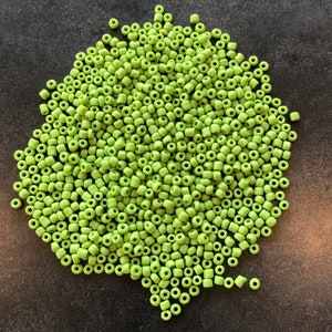 May include: A large pile of small, round, green glass beads. The beads are all the same size and shape, and they are arranged in a random pattern.