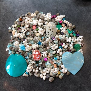 May include: A collection of small white, blue, and green seashells, beads, and other decorative elements. There are two larger seashells, one turquoise and one light blue, in the shape of a heart and a circle.