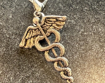 May include: Silver-toned charm featuring the Caduceus symbol, a staff with two snakes entwined around it, topped with wings. The charm has a lobster clasp for easy attachment to a bracelet or necklace. The medical symbol is a great gift for doctors and nurses.