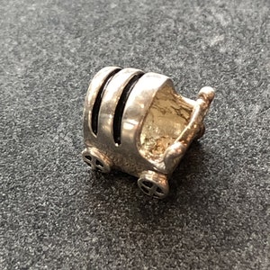 May include: Silver charm in the shape of a baby carriage with black accents. The carriage has four wheels and a handle.