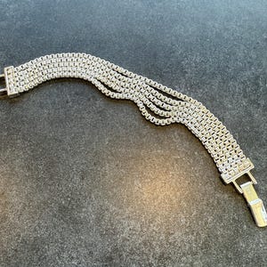 May include: Silver-toned bracelet featuring a multi-strand design. The bracelet has a rectangular clasp and is composed of small, interconnected square links. The overall style is elegant and suitable for various occasions.