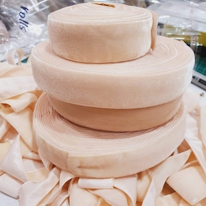 以下が含まれることがあります： ベージュのベルベットリボンが4つ重ねられています。リボンは柔らかく高級感があり、クラフトやデコレーションに最適です。