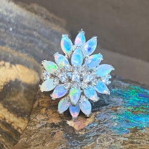 May include: A white opal ring with a flower design. The ring is set in silver and features a cluster of white opals and small diamonds.